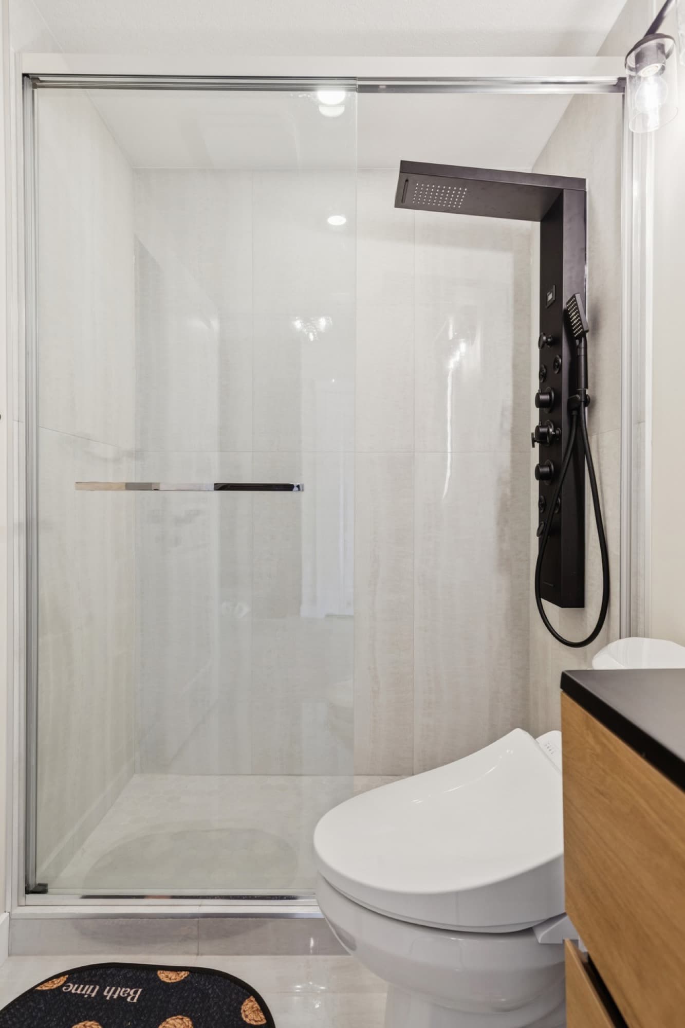 Basement bathroom with glass shower, black rain panel and wood vanity
