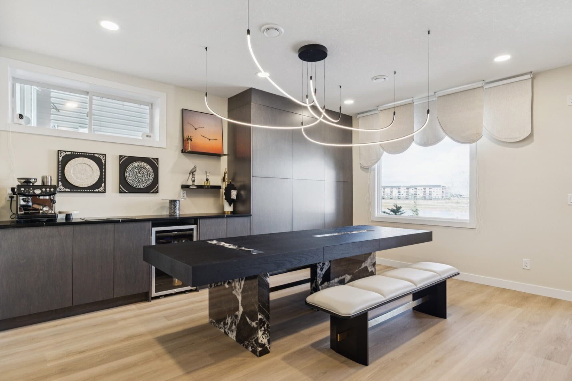 Basement coffee bar and black-marble dining table under a curved LED chandelier