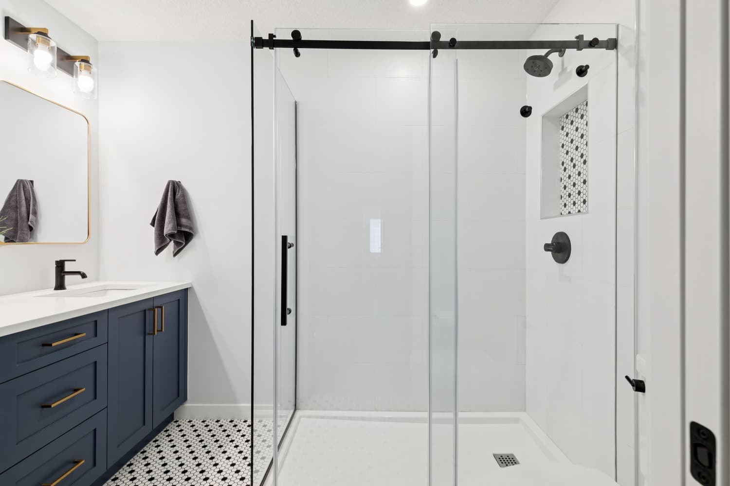 Suite bathroom with navy vanity, glass walk-in shower and mosaic tile floor