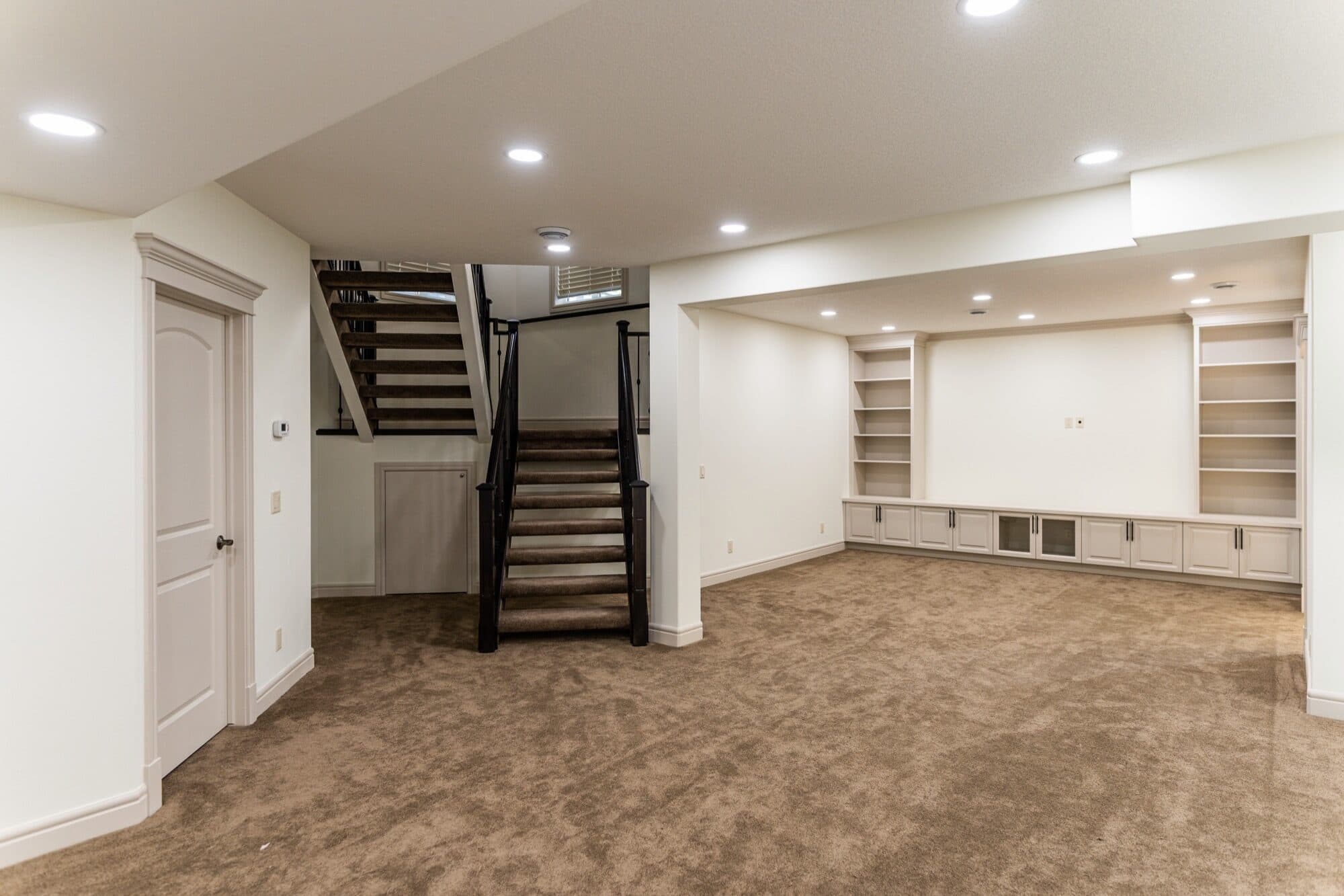 Wide open finished basement with built-in shelving and staircase