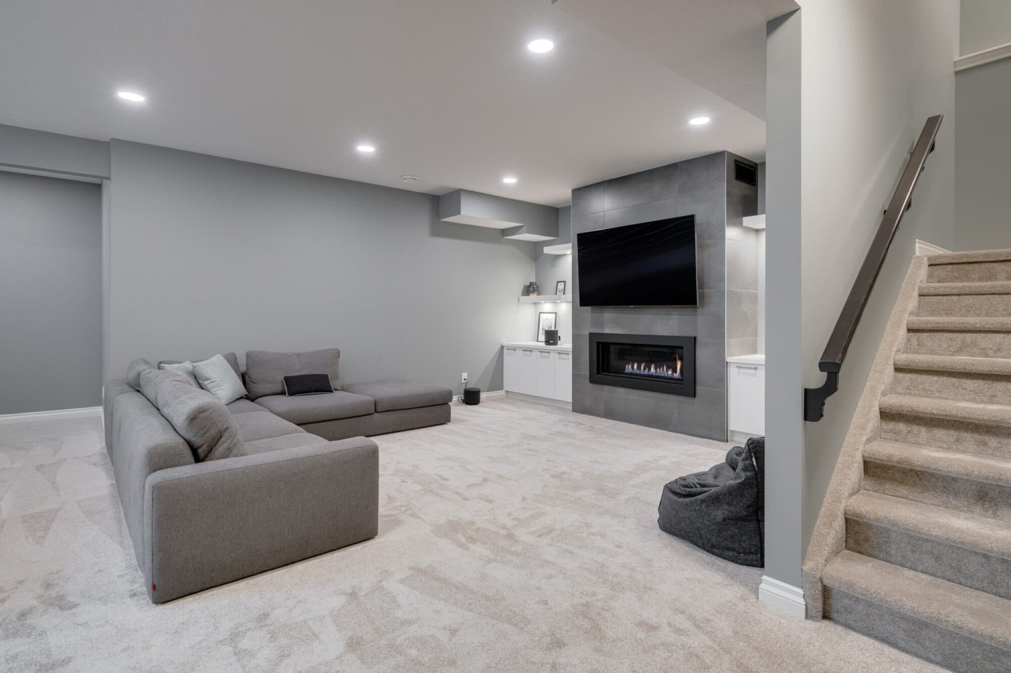Grey basement rec room with linear fireplace and built-in cabinetry
