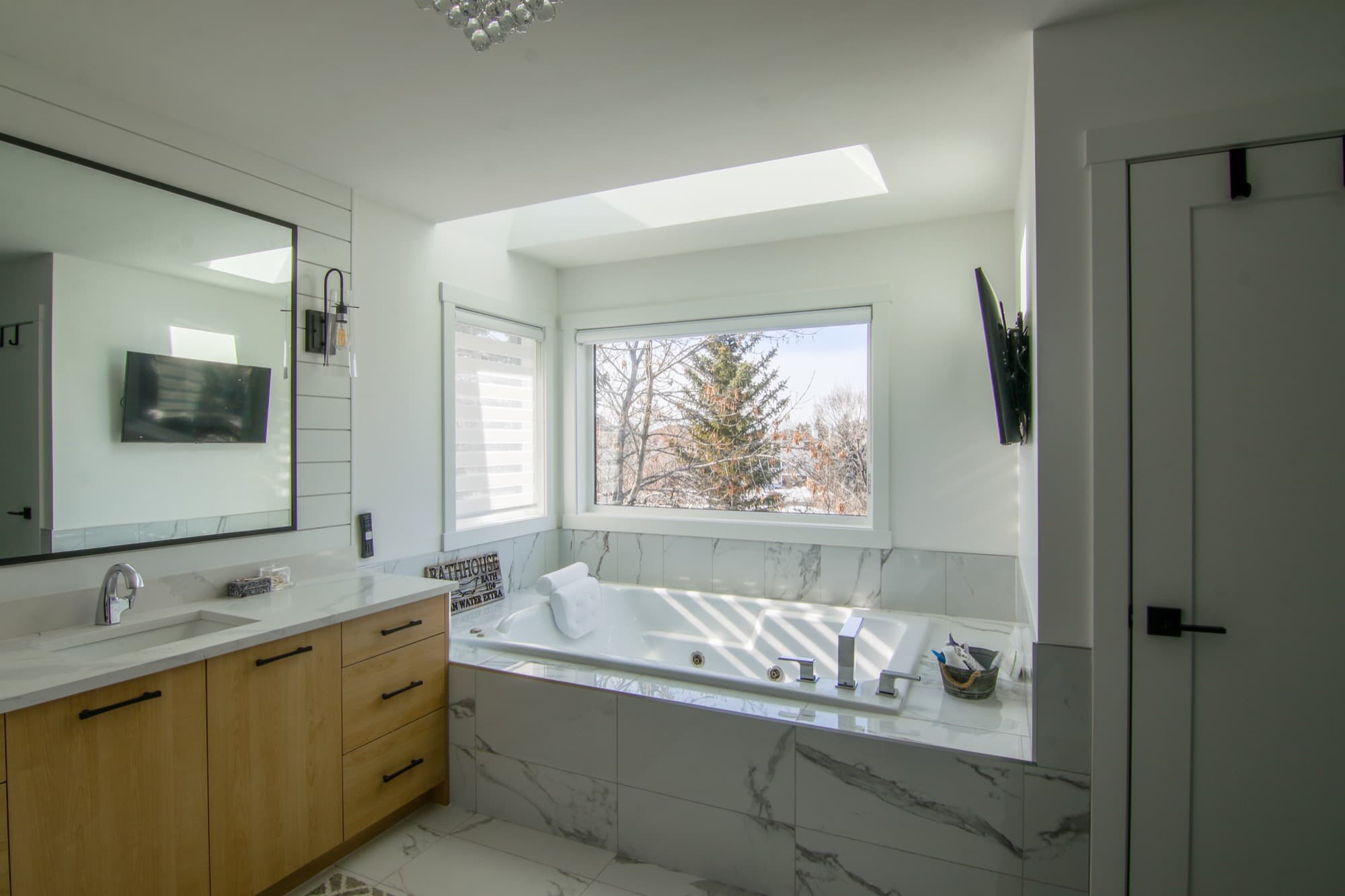 Bright primary bathroom with soaker tub, skylight and wood vanity