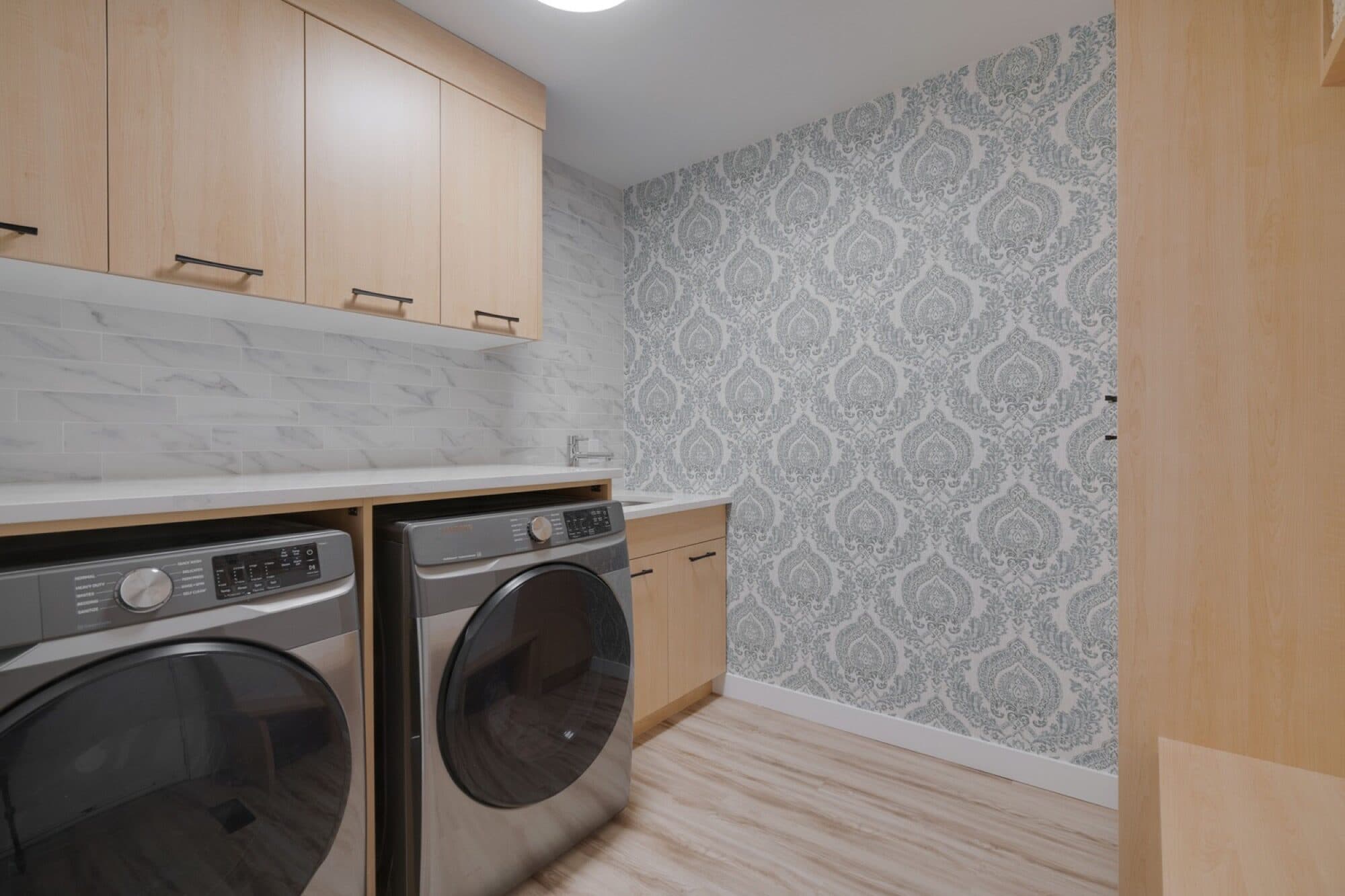 Laundry room with light oak cabinets and damask wallpaper