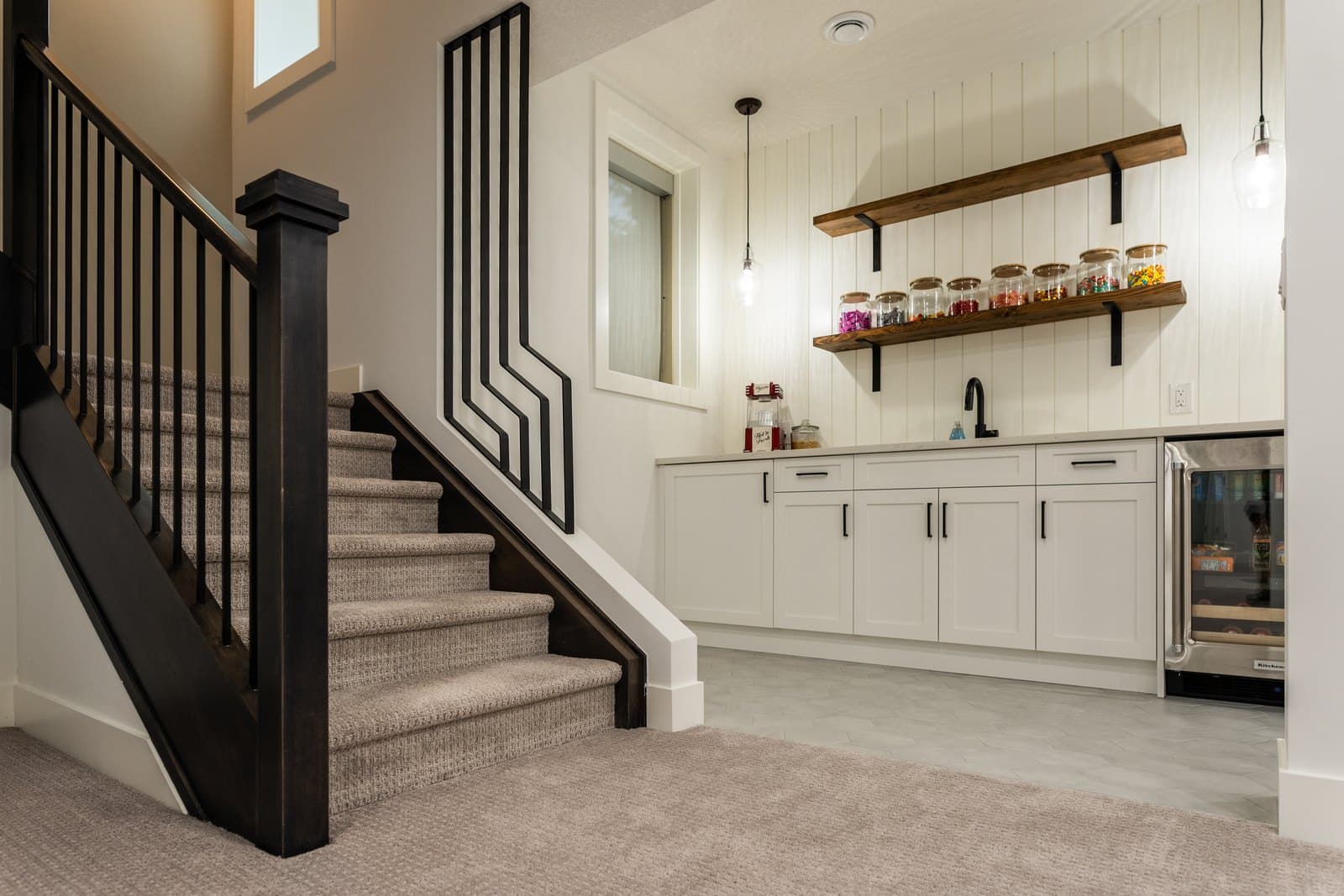 A finished mid-range Calgary basement by ReImagine Builders with a custom staircase, wet bar and beverage fridge
