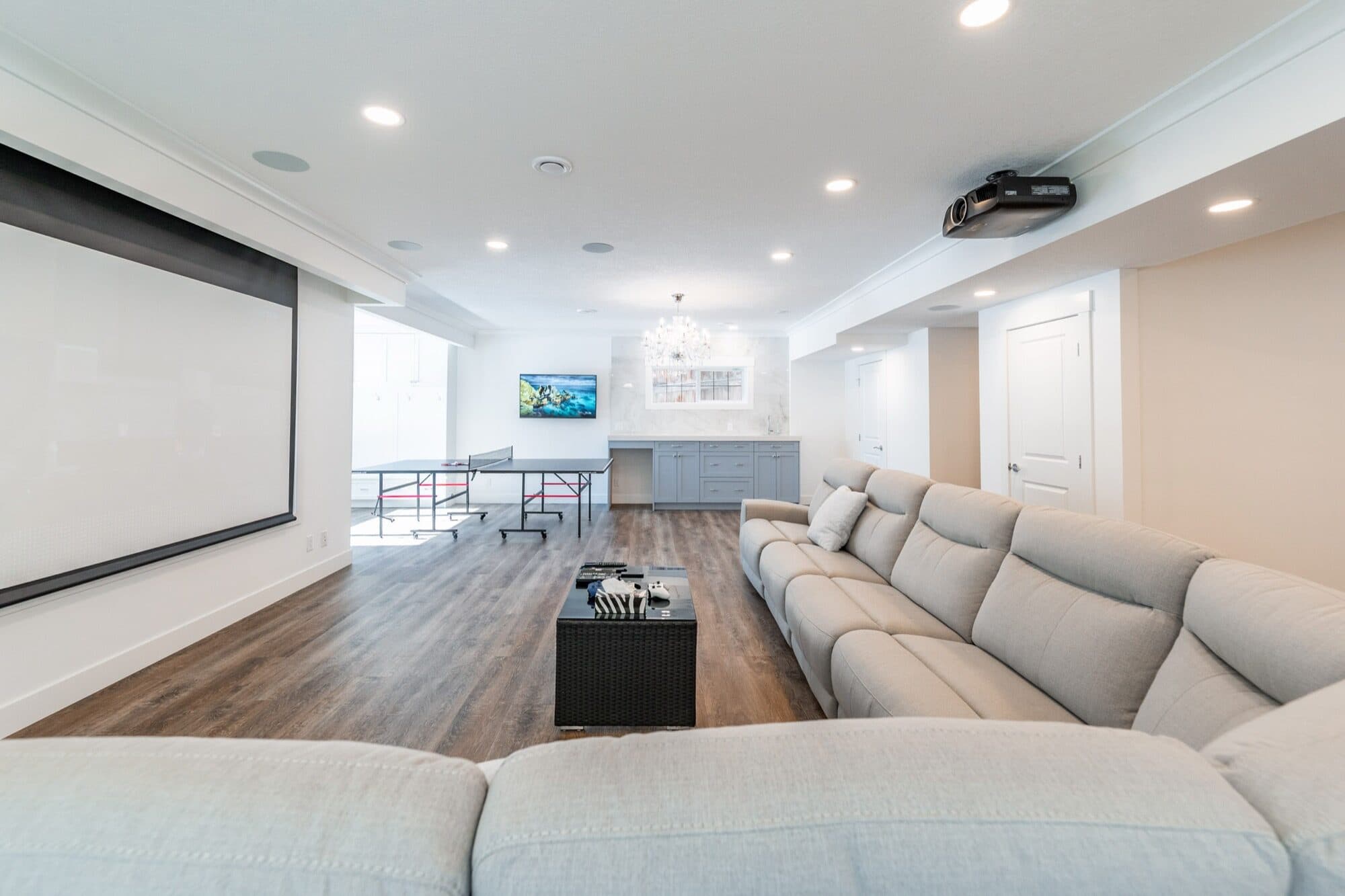 Finished Calgary basement home theatre with projector screen, ping-pong table and sectional